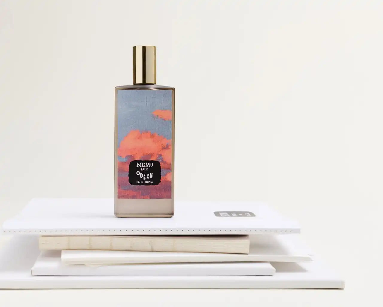 A rectangular glass perfume bottle with a golden cap and a label depicting a cloudy sunset.
