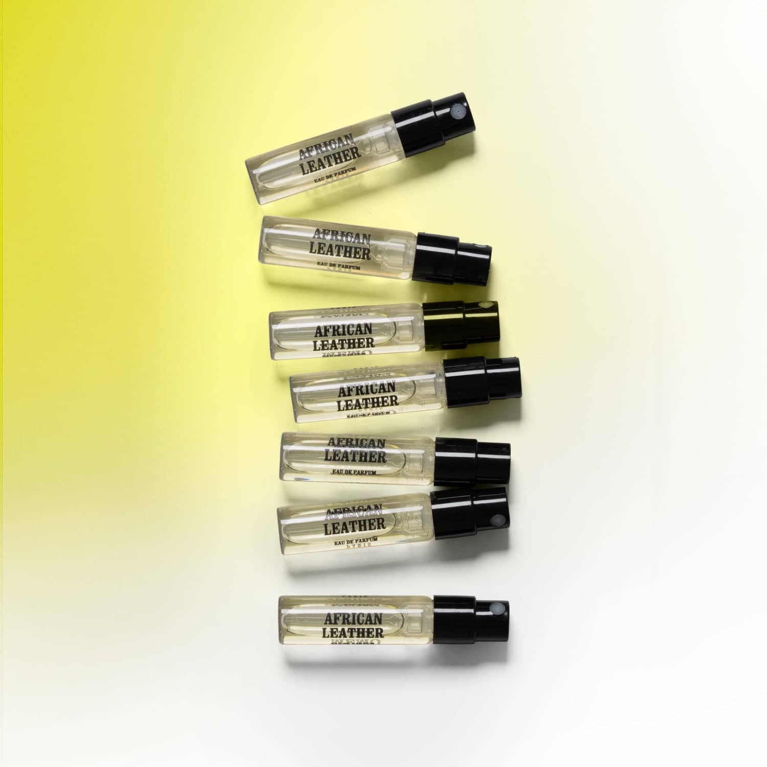 Six transparent glass vials of african leather eau de parfum, each with a black spray nozzle and minimalist label.