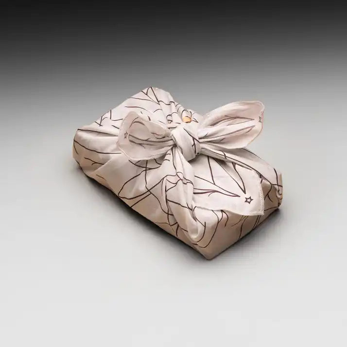 A light-colored fabric gift wrap with a dark, abstract pattern tied with a bow.