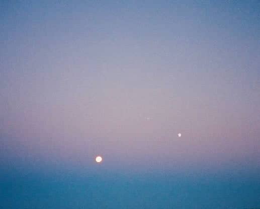 A soft twilight sky with a pale pink and blue gradient, featuring two faintly glowing celestial bodies.